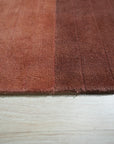 Isla Striped Rust Hand Tufted Wool Rug displayed on a polished wood floor, showcasing its warm rust tones and bold stripe design within a contemporary living space.