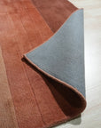 Isla Striped Rust Hand Tufted Wool Rug, its warm rust hues and textured wool stripes creating a cozy, inviting ambiance in a naturally lit living space with neutral furniture.