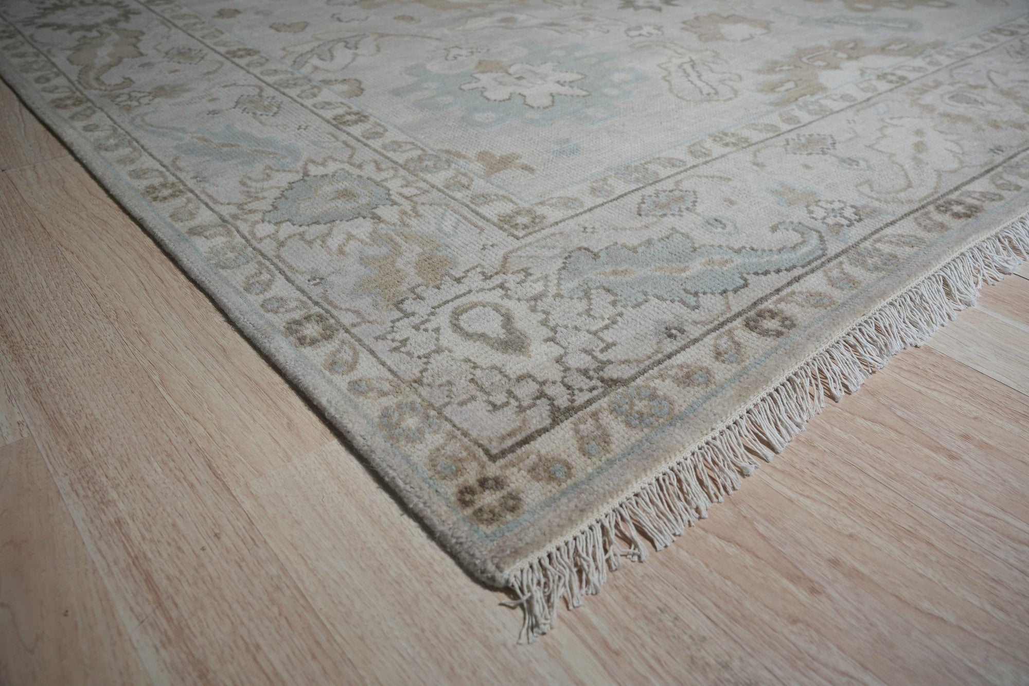 Classic Tessa Beige Nan Rug, its intricate geometric pattern rendered in soft beige tones, lying elegantly on a light wood floor, suggesting a warm and inviting atmosphere.