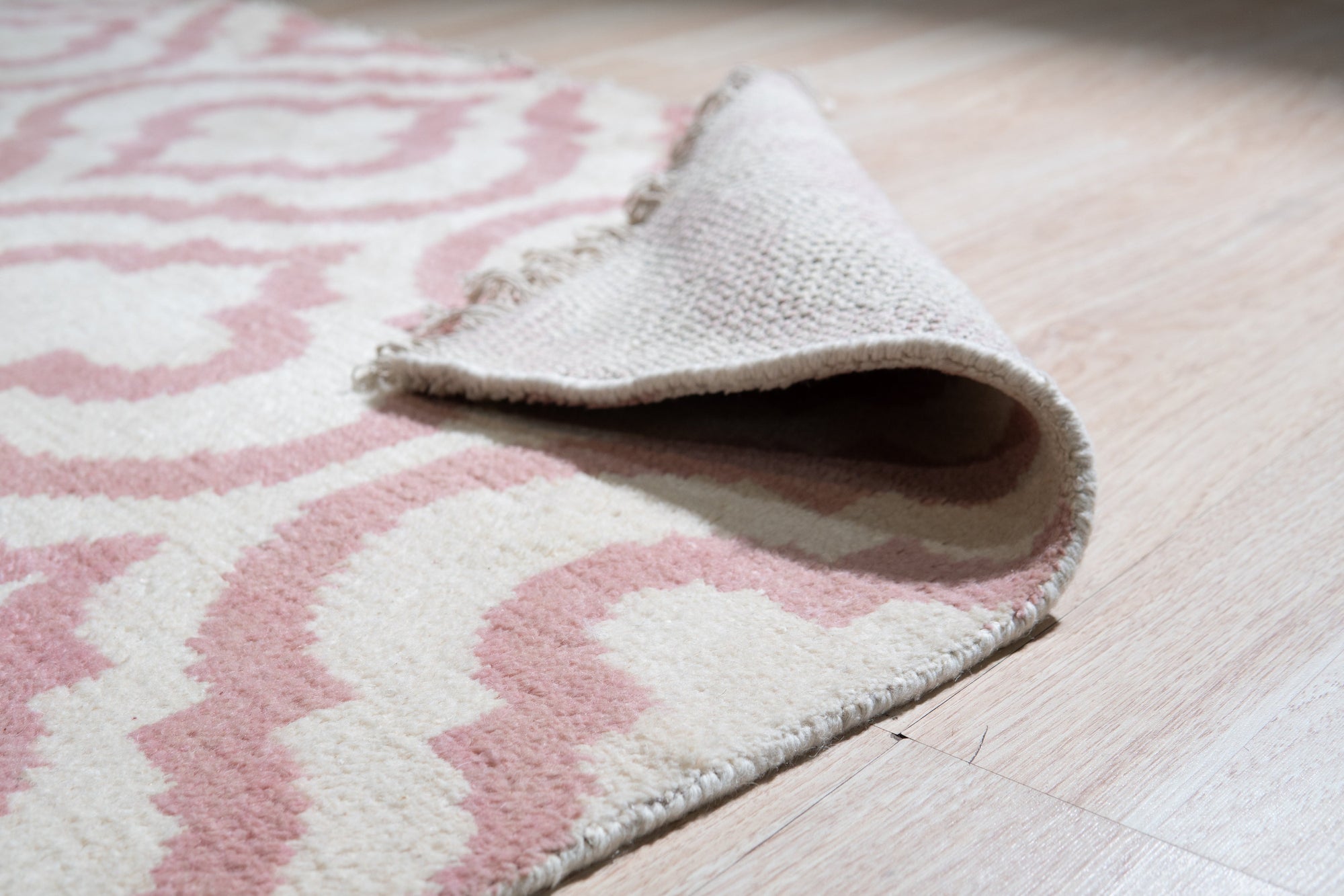 Inviting Moroccan Pink Hand Knotted Wool Rug, its blush and cream hues softening a brightly lit living space; intricate geometric patterns hand-knotted in wool bring a warm, textural element to the modern decor.
