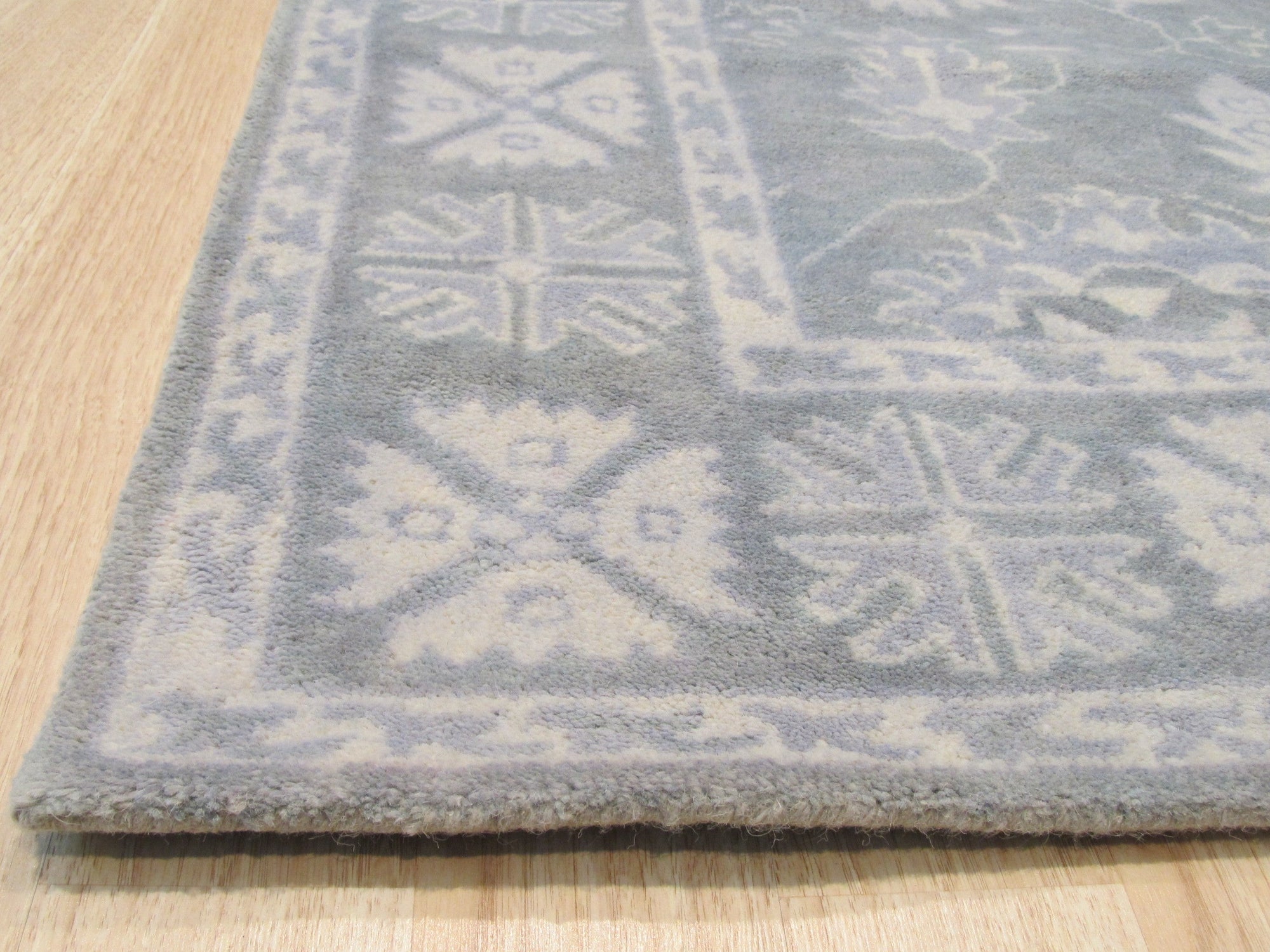 Louie Oriental Gray Hand Tufted Wool Rug, its intricate traditional patterns rendered in cool grays and creams, lies grounded on a light wood floor, creating a sophisticated contrast. Soft texture and durable wool construction are visually apparent.