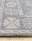 Louie Oriental Gray Hand Tufted Wool Rug, its intricate traditional patterns rendered in cool grays and creams, lies grounded on a light wood floor, creating a sophisticated contrast. Soft texture and durable wool construction are visually apparent.