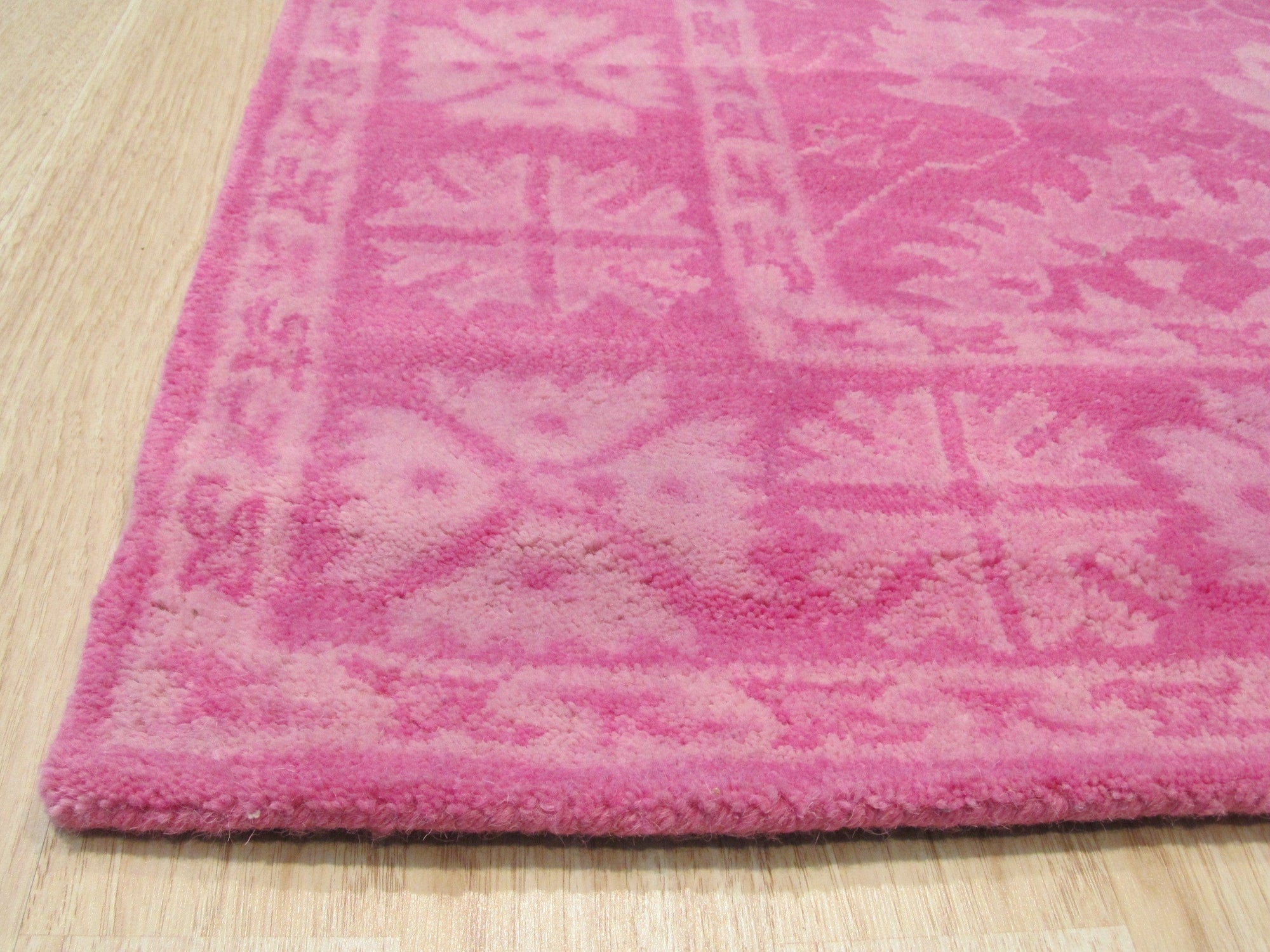 Opulent Oriental Pink Hand Tufted Wool Rug, featuring intricate floral patterns in shades of pink and cream, rests gracefully on a light-colored floor, lending warmth and elegance to the space.
