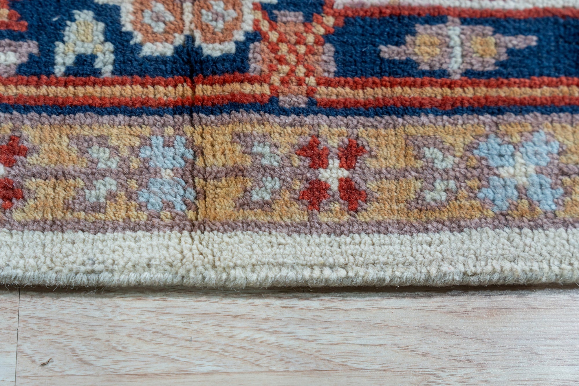 Classic Elegant Blue Hand-Knotted Wool Rug, with intricate floral patterns and a rich blue hue, lies on a light wood floor, partially under a wooden table with books and decor, suggesting a sophisticated living space.