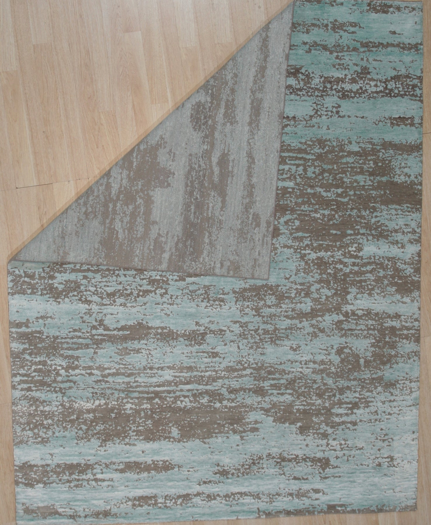Amara Captivating Silver Hand Knotted Wool Rug, showcasing its intricate pattern of geometric and floral motifs in shimmering silvers and soft creams, resting in a bright living room setting.