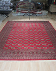 Rustic Nina Red Nan Rug, a vibrant red area rug featuring a distressed, vintage-inspired design, lies flat showcasing its intricate woven texture and short fringe detail. Warm lighting highlights the rug's subtle variations in tone.