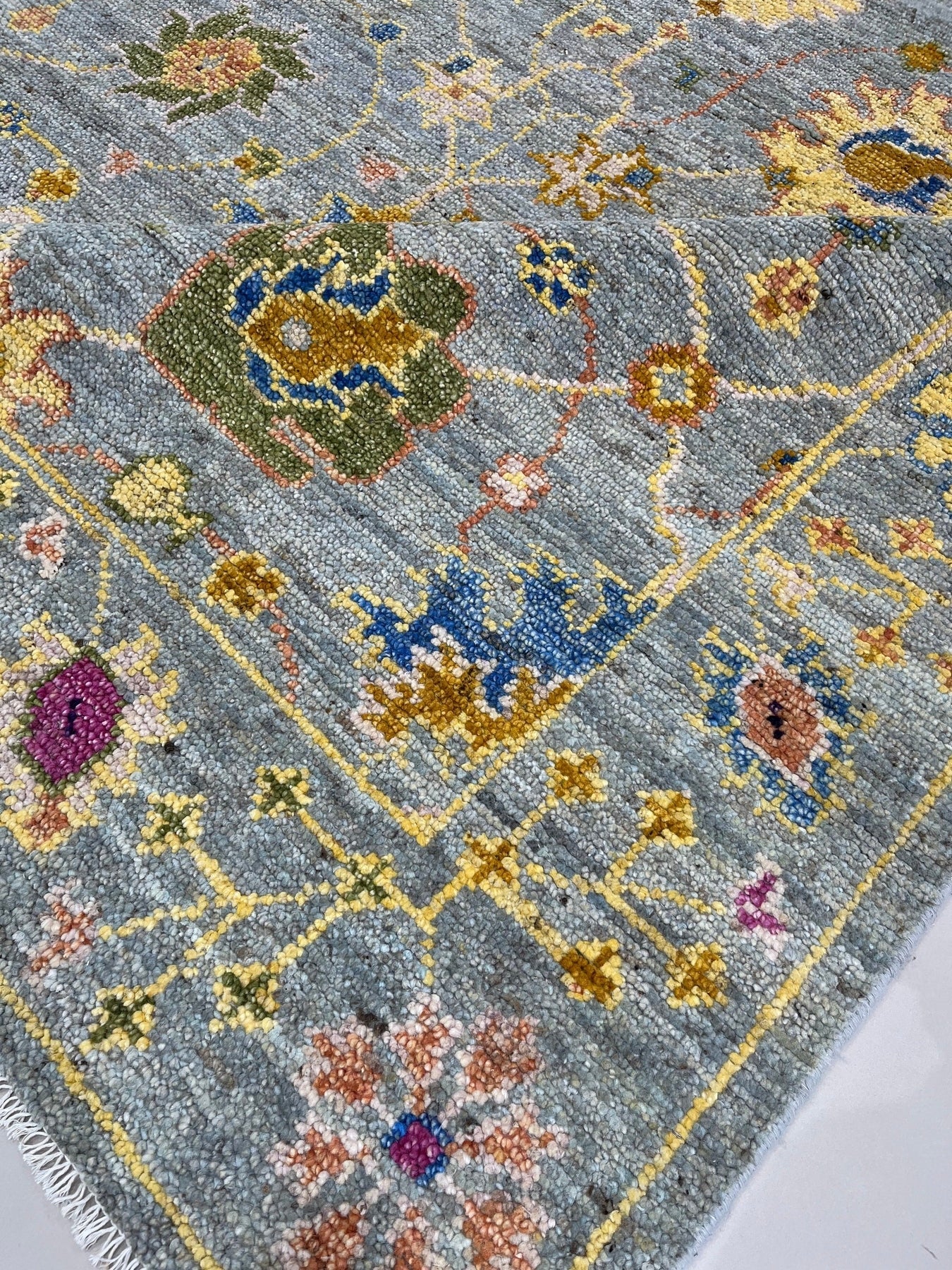 Talia Lila Gray Hand Knotted Wool Rug, displaying intricate patterns and subtle color variations, rests in a brightly lit interior, showcasing its texture and design alongside modern furniture.