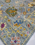 Talia Lila Gray Hand Knotted Wool Rug, displaying intricate patterns and subtle color variations, rests in a brightly lit interior, showcasing its texture and design alongside modern furniture.