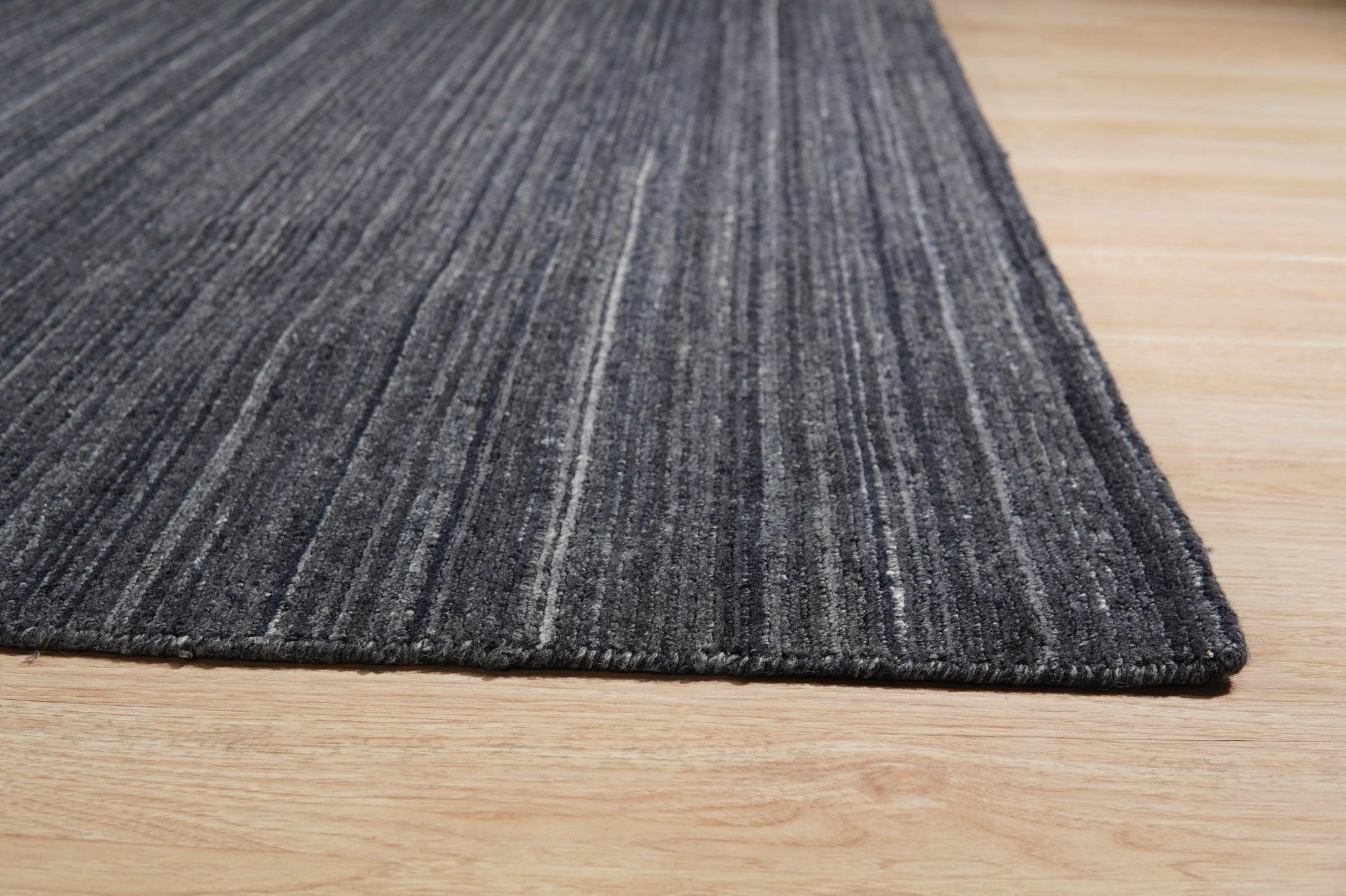 Delicate Striped Charcoal Handmade Wool Rug, presenting charcoal and ivory stripes in a handwoven wool construction, lies flat on a light surface, accentuating its subtle texture and refined color palette.