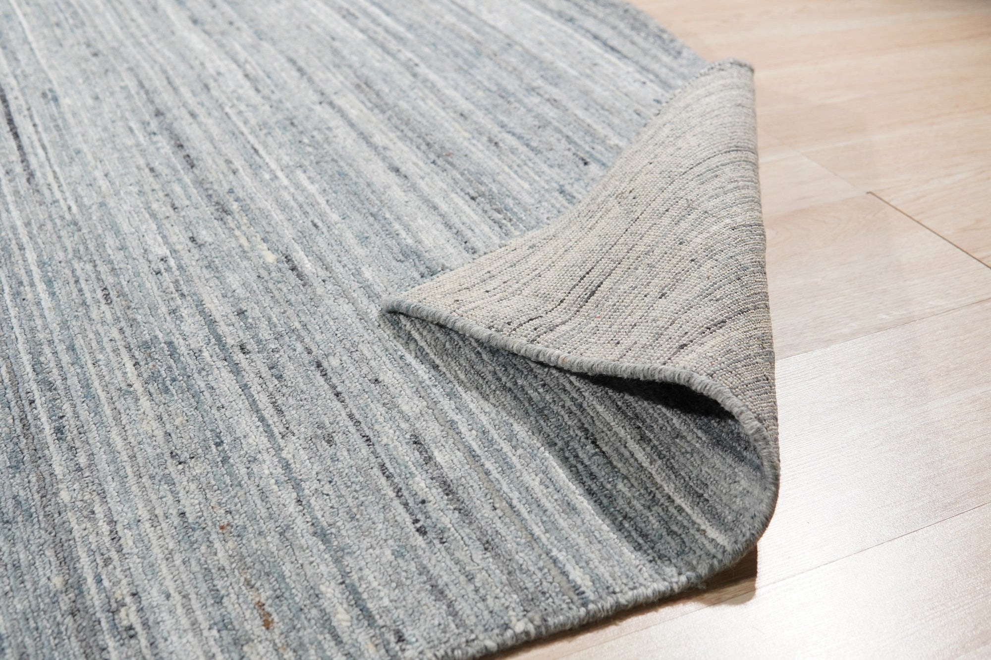 Delicate Striped Gray Handmade Wool Rug displayed in a bright room; its gray and cream stripes offer a subtle, textural contrast, highlighting the rug's handmade wool construction and soft, inviting appearance.