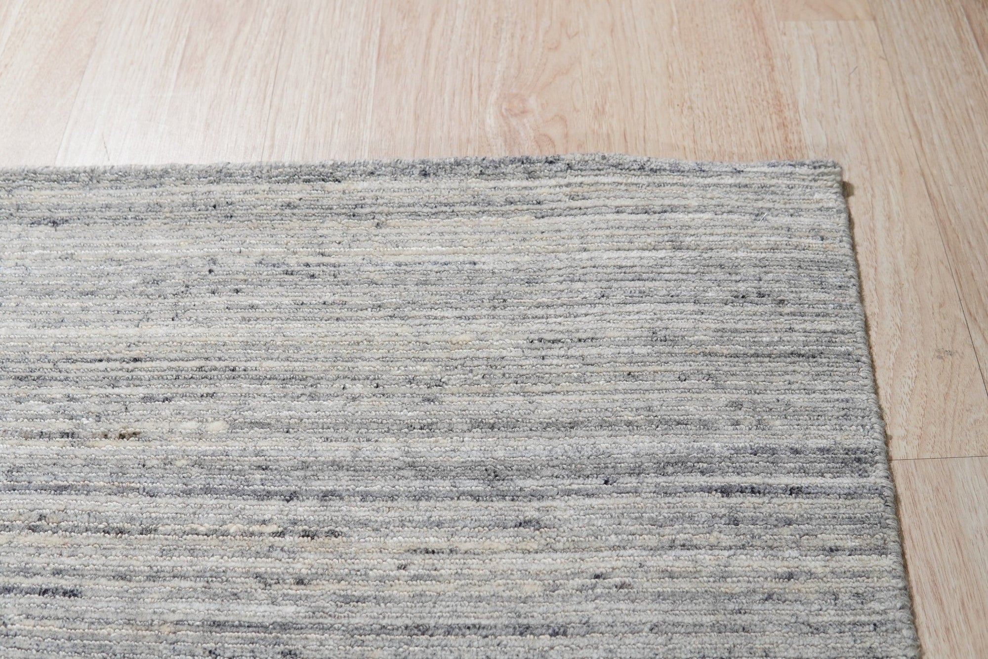 Delicate Striped Ivory Handmade Wool Rug, its soft ivory stripes creating a calming rhythm on the handwoven wool texture, showcased on hardwood flooring in a brightly lit space.