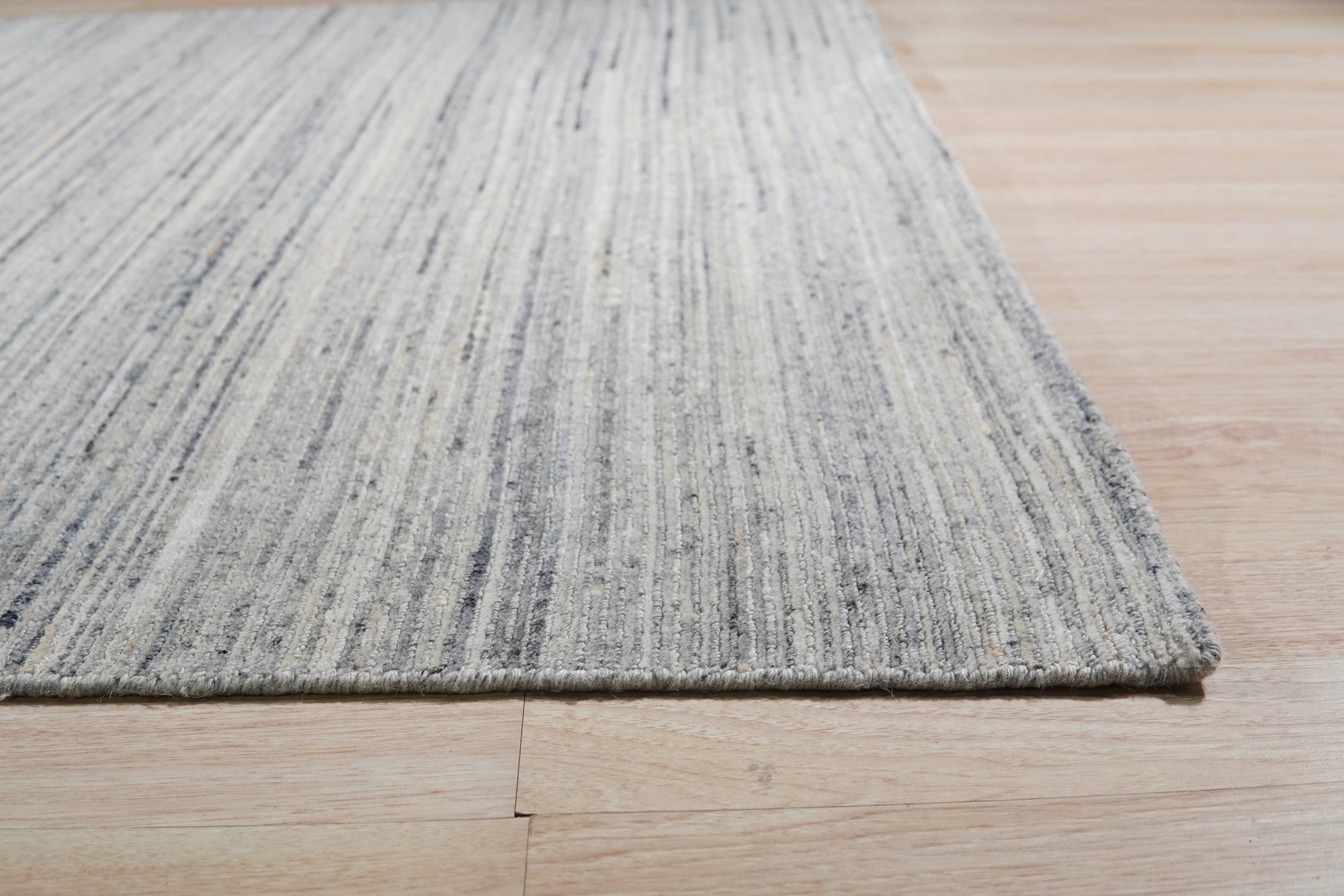 Delicate Striped Ivory Handmade Wool Rug, showcasing its subtly striped pattern and soft ivory hue, laid on a light wood floor with warm, inviting light emphasizing the wool's texture.