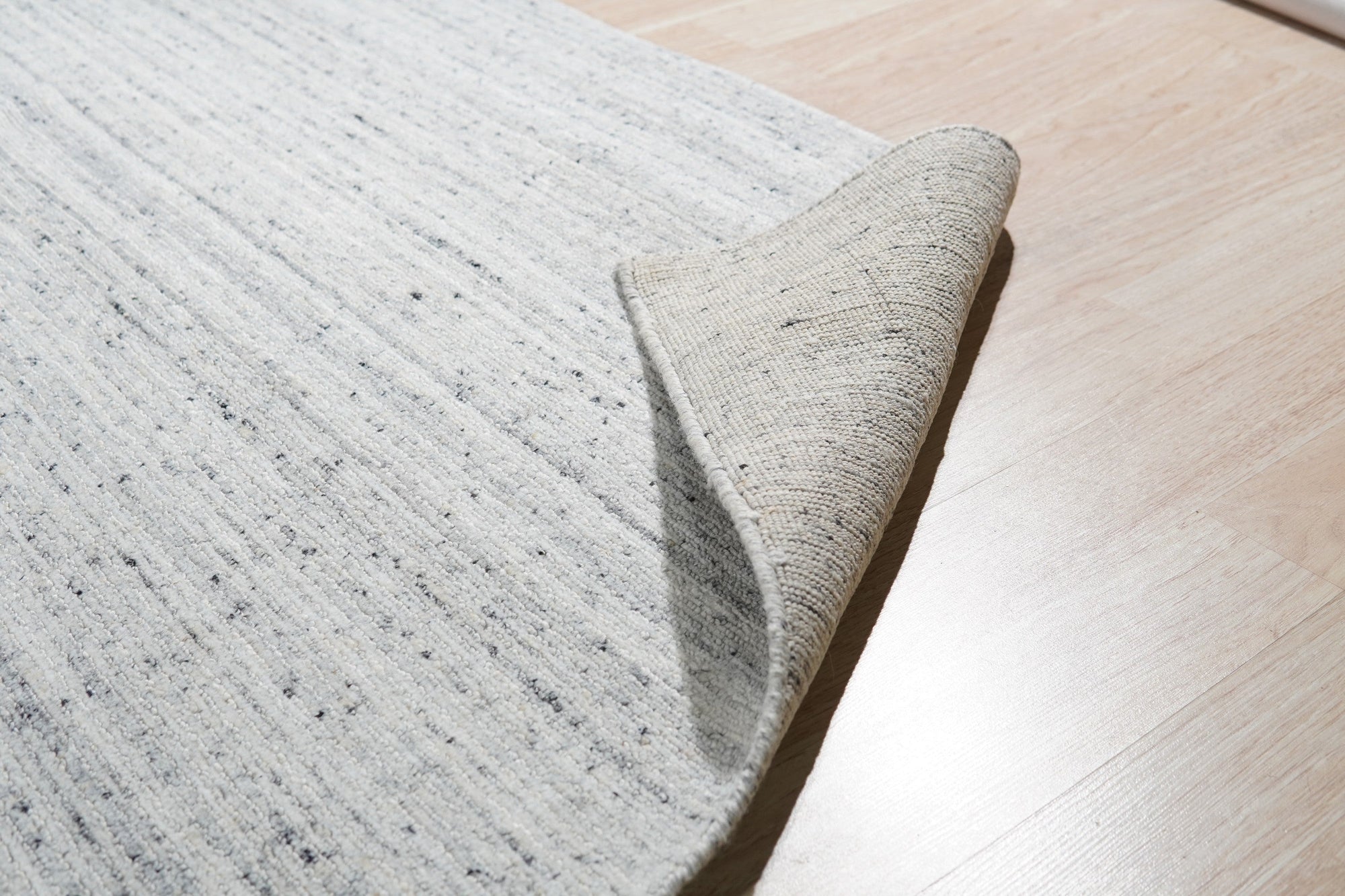 Delicate Striped Silver Handmade Wool Rug, its subtle silver stripes cascading across a soft wool surface, showcased as a design element in an interior setting.