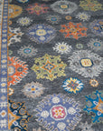 Lila Ruby Charcoal Hand Knotted Wool Rug, featuring subtly shifting charcoal and ruby tones, graces a light-filled room with hardwood floors and a woven basket, illustrating its potential as a grounding, elegant element.