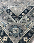Maya Oushak Silver Hand Knotted Wool Rug, showcasing a silvery-grey palette and intricate floral patterns woven in hand-knotted wool, lies gracefully on the floor in a warmly lit interior space.
