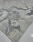 Lydia Cassandra Gray Hand Knotted Wool Rug, featuring a subtly patterned gray surface with textural variations, displayed in a well-lit interior setting highlighting its soft, neutral tones and hand-knotted construction.