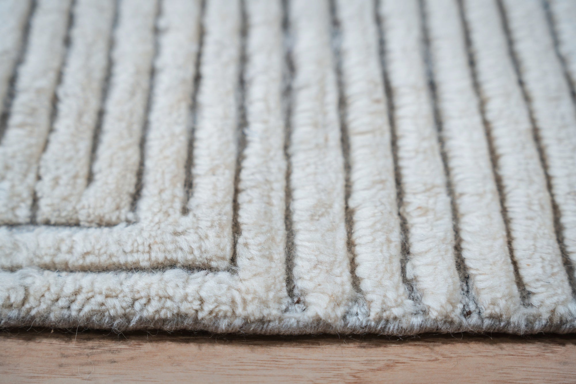 Celia Lila Ivory Hand Knotted Wool Rug, showcasing a subtle lilac and ivory palette with intricate hand-knotted detailing, lies elegantly on a hardwood floor in a naturally lit room, inviting warmth and texture.