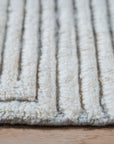 Celia Lila Ivory Hand Knotted Wool Rug, showcasing a subtle lilac and ivory palette with intricate hand-knotted detailing, lies elegantly on a hardwood floor in a naturally lit room, inviting warmth and texture.