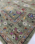 Ophelia Oriental Green Hand Knotted Wool Rug, a richly detailed expanse of emerald, sage, and ivory wool, its intricate hand-knotted patterns bringing timeless elegance to a warmly lit living space.