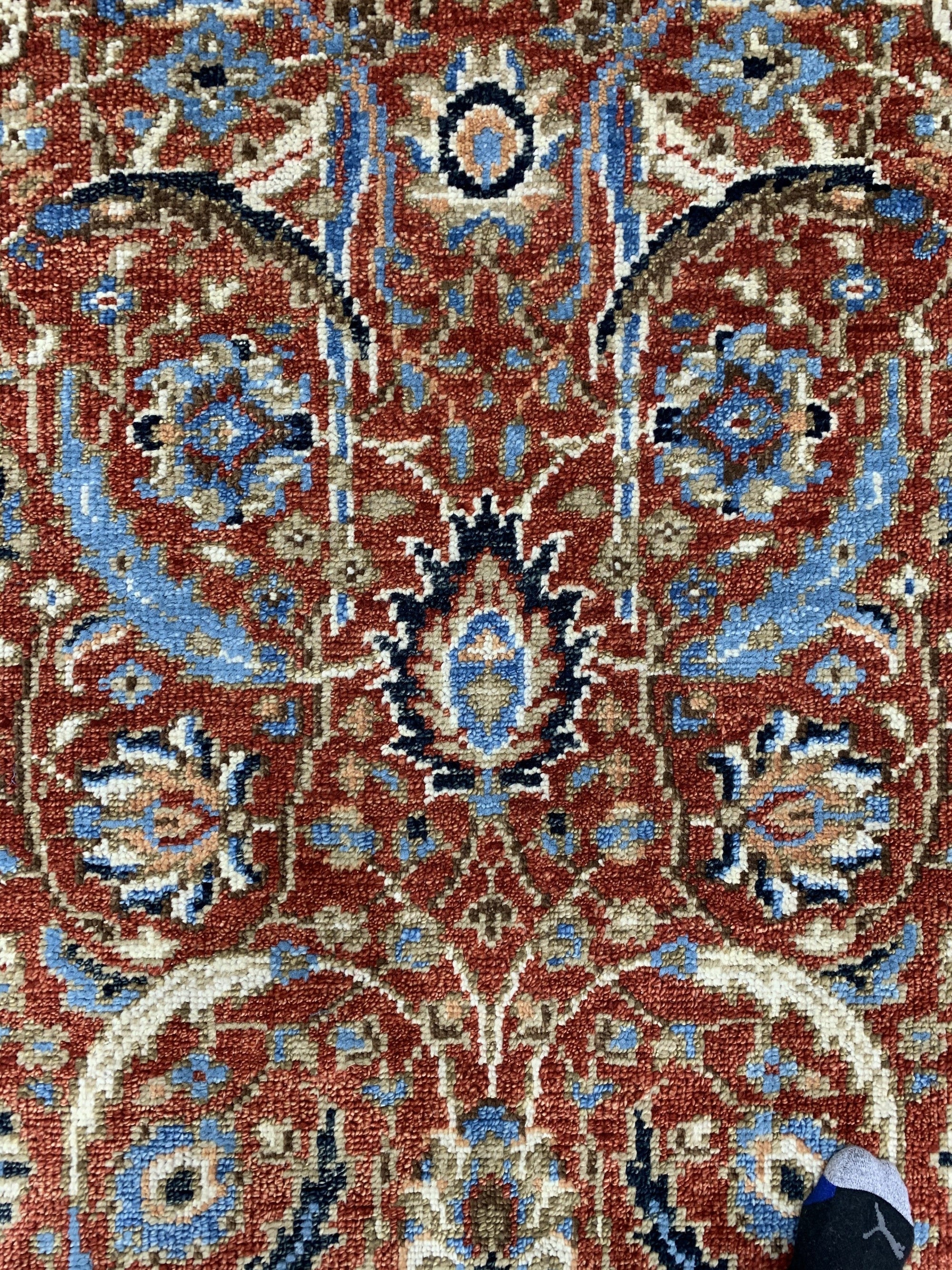 Rustic Oriental Red Hand Knotted Wool Rug displayed on a light wood floor. The hand-knotted construction is evident in its intricate, traditional Oriental pattern in shades of red, cream, and navy. Warm, inviting texture promises comfort and style.