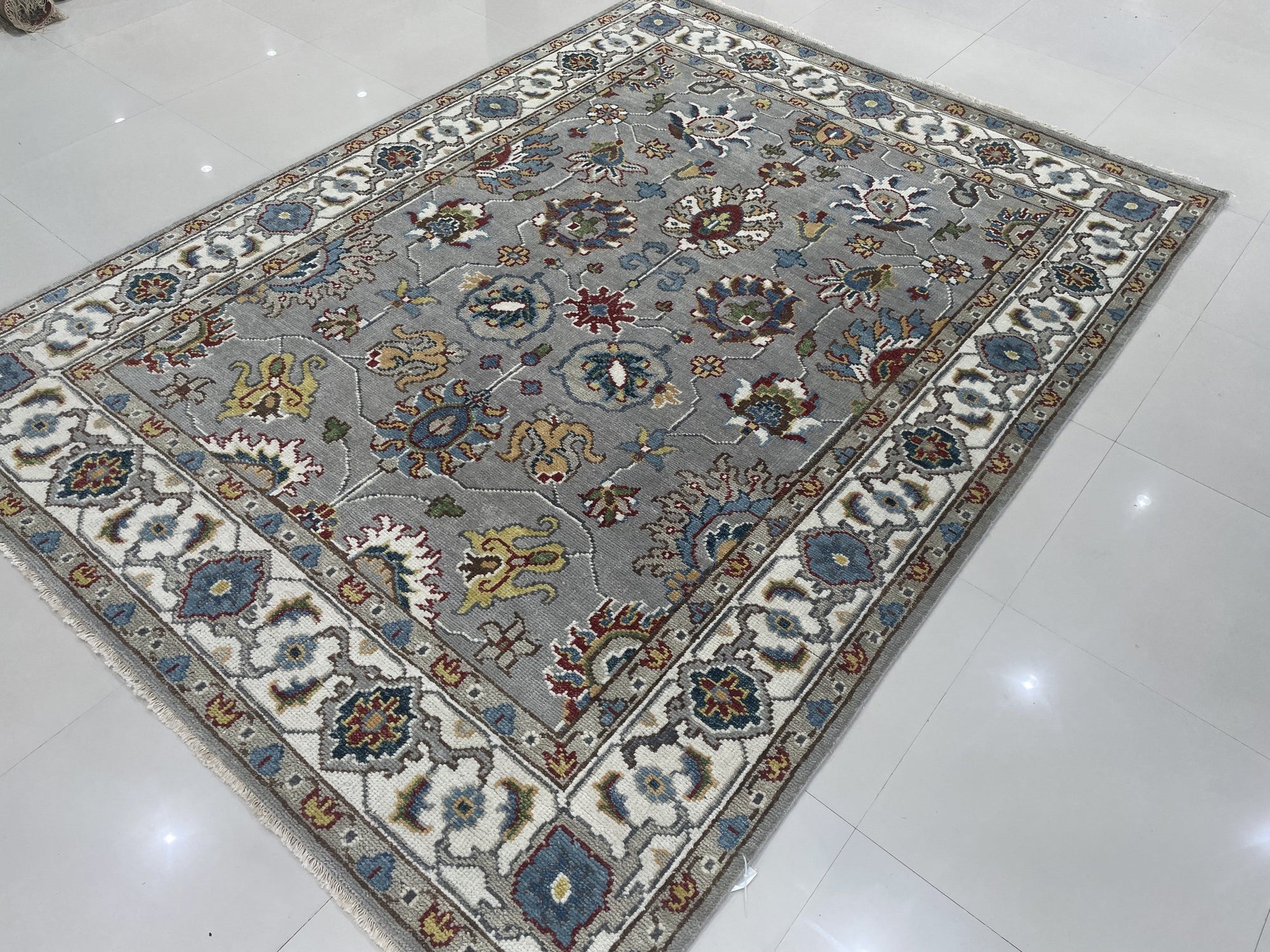 Enchanting Oriental Gray Hand Knotted Wool Rug, showcasing its intricate gray and cream pattern and hand-knotted wool construction, rests elegantly on a polished hardwood floor.