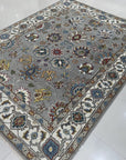 Enchanting Oriental Gray Hand Knotted Wool Rug, showcasing its intricate gray and cream pattern and hand-knotted wool construction, rests elegantly on a polished hardwood floor.