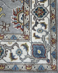 Enchanting Oriental Gray Hand Knotted Wool Rug, featuring intricate floral and geometric patterns in shades of gray and ivory, lies flat on a light-colored floor, its hand-knotted wool construction creating a soft and inviting texture.