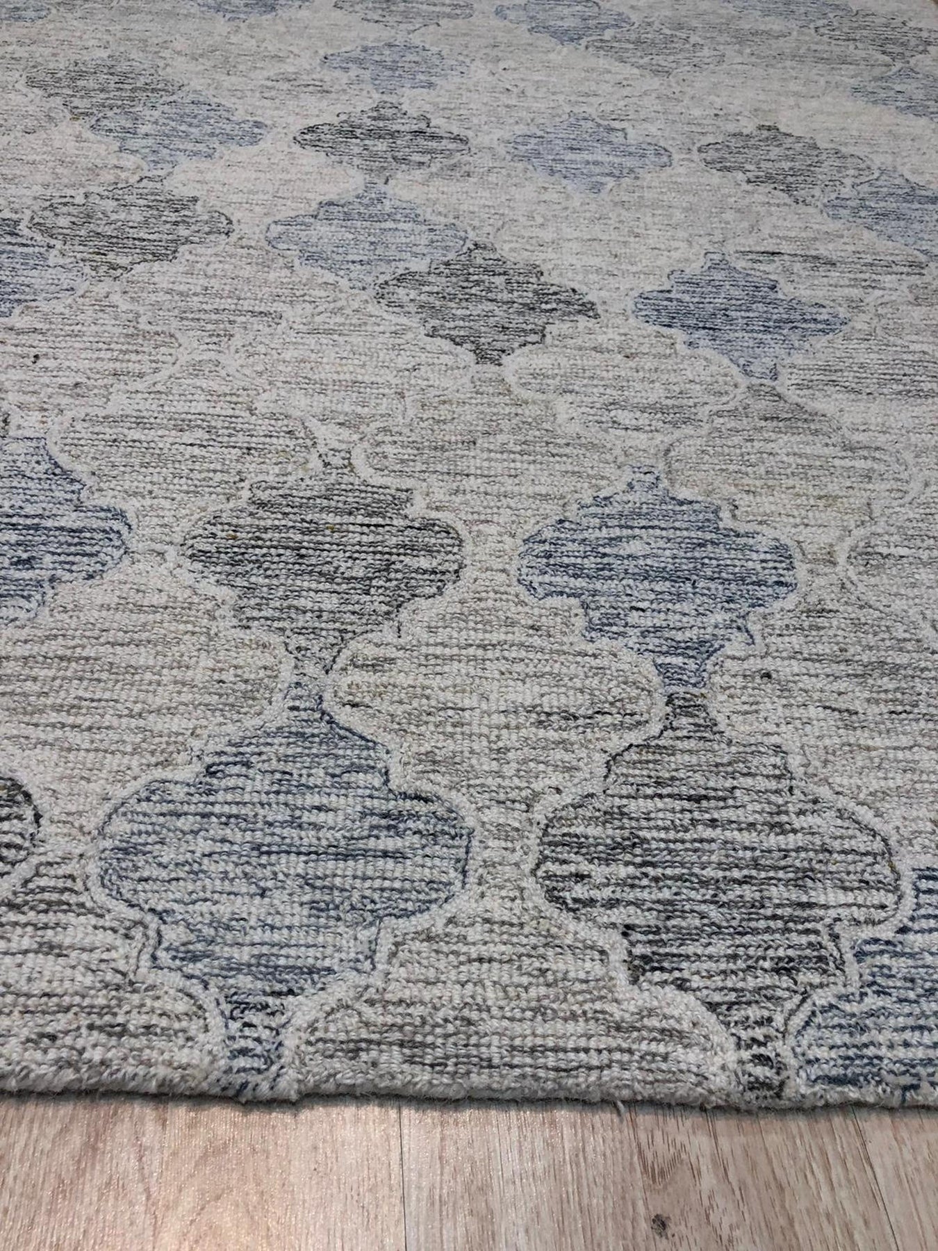 Zinnia Kira Multicolor Hand Tufted Wool Rug, vibrant blend of colors and textures pops against a light wooden floor. Detailed hand-tufted construction reveals intricate floral motifs and geometric patterns. Warmth and artistry radiate from this wool rug, inviting touch and enhancing the room's décor.