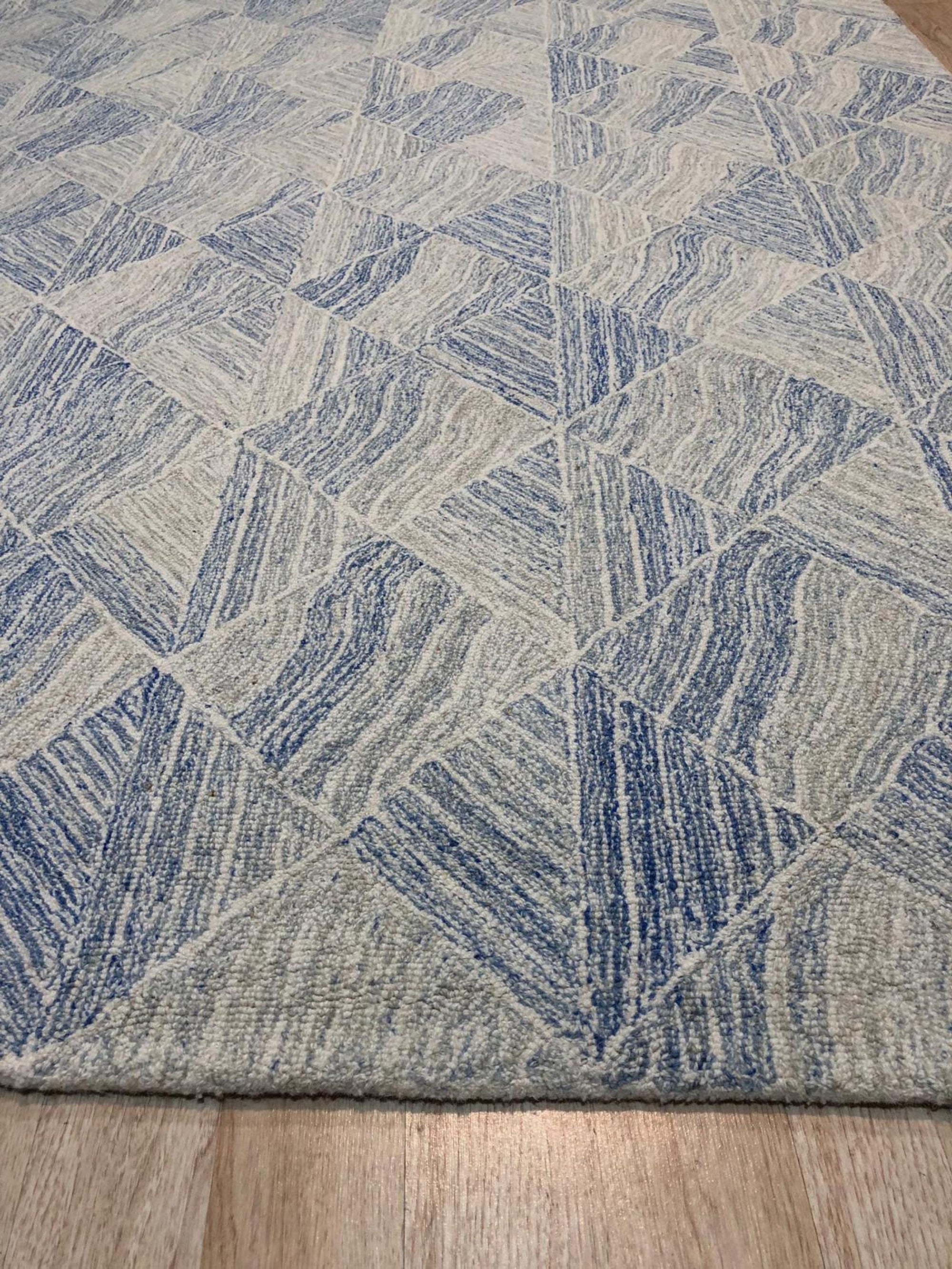 Trara Nadia Blue Hand Tufted Wool Rug, a captivating blend of cool blues and subtle creams, offers a luxurious underfoot experience with its hand-tufted wool construction, presented in a room setting that highlights its calming presence.