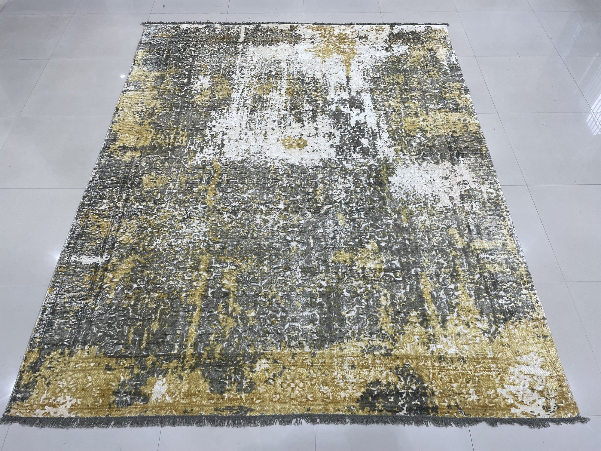 Chic Iris Gold Hand Knotted Wool Rug, its shimmering gold threads catching the light, lies elegantly on a dark hardwood floor, adding warmth and sophisticated texture to the room.