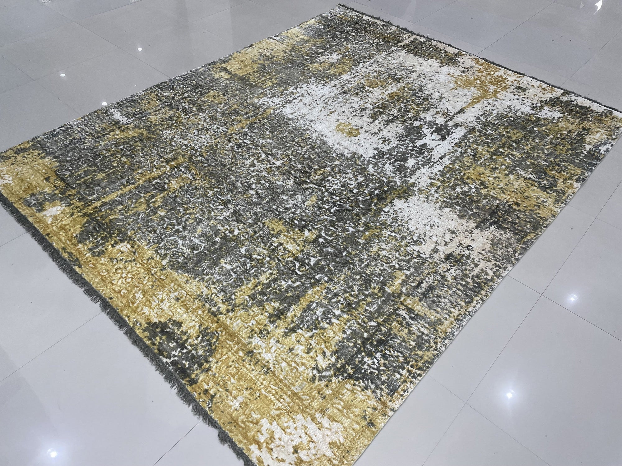 Chic Iris Gold Hand Knotted Wool Rug, shimmering with gold threads and intricate floral patterns, lies elegantly on a light wood floor, creating a warm and inviting atmosphere.