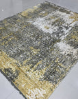 Chic Iris Gold Hand Knotted Wool Rug, shimmering with gold threads and intricate floral patterns, lies elegantly on a light wood floor, creating a warm and inviting atmosphere.