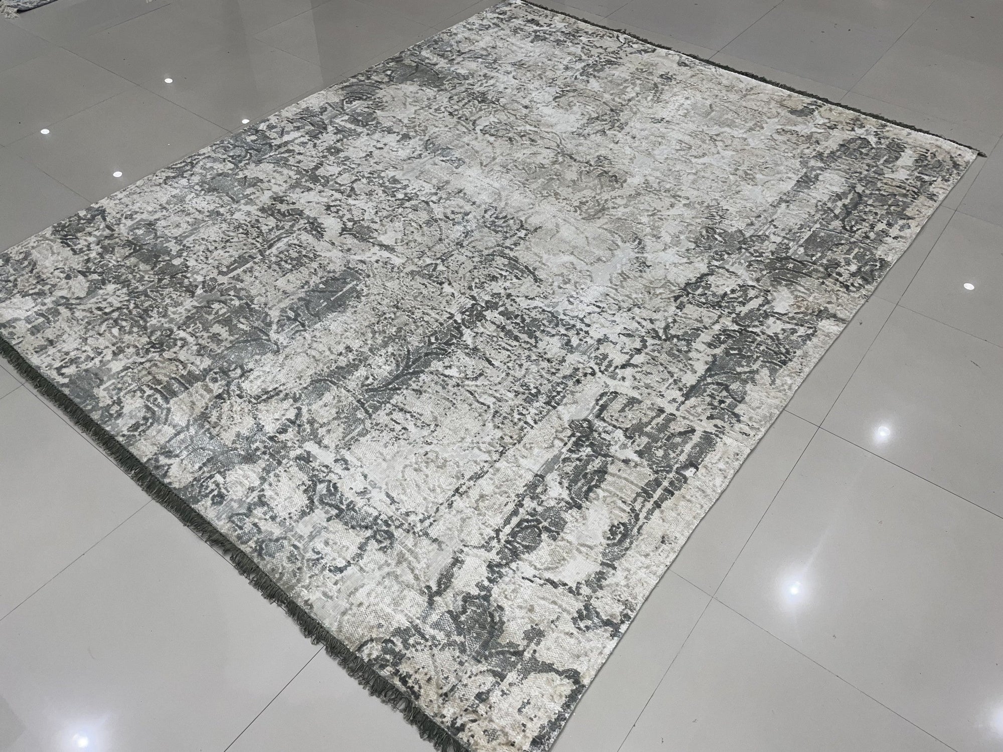 Sarrah Penelope Gray Hand Knotted Wool Rug, showcasing a muted gray palette and intricate hand-knotted details, rests softly on a light wood floor, its texture inviting a touch of warmth and sophistication.