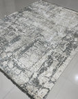 Sarrah Penelope Gray Hand Knotted Wool Rug, showcasing a muted gray palette and intricate hand-knotted details, rests softly on a light wood floor, its texture inviting a touch of warmth and sophistication.