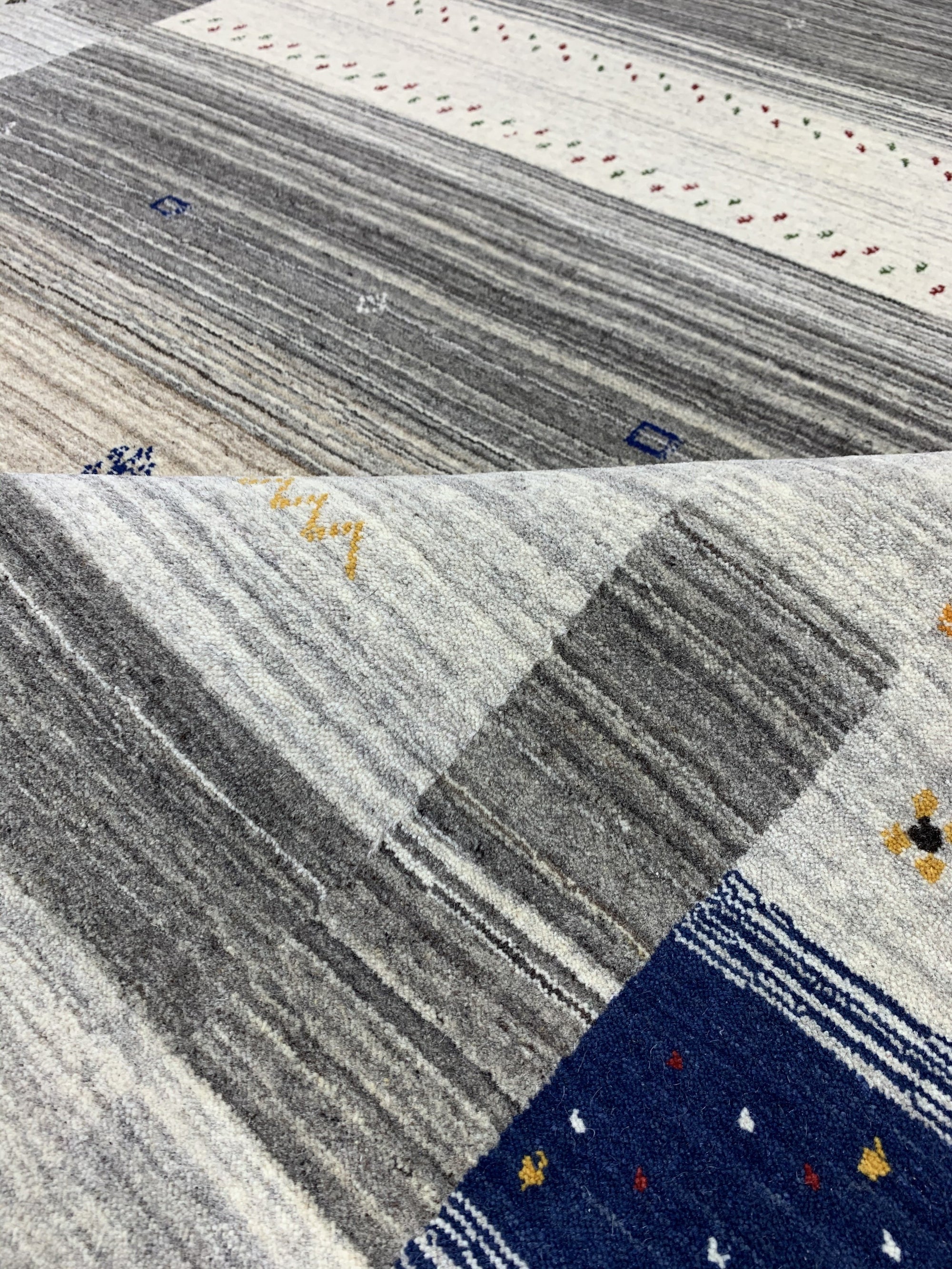 Classic Gabbeh Multicolor Hand Knotted Wool Rug, vibrant stripes of red, orange, yellow, green, blue, and purple create a playful and textured floor covering in a brightly lit interior.