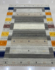 Here's the alt text based on the provided information:
Classic Gabbeh Multicolor Hand Knotted Wool Rug, vibrant stripes of red, blue, yellow, and green hues bring warmth and texture to a neutral floor.