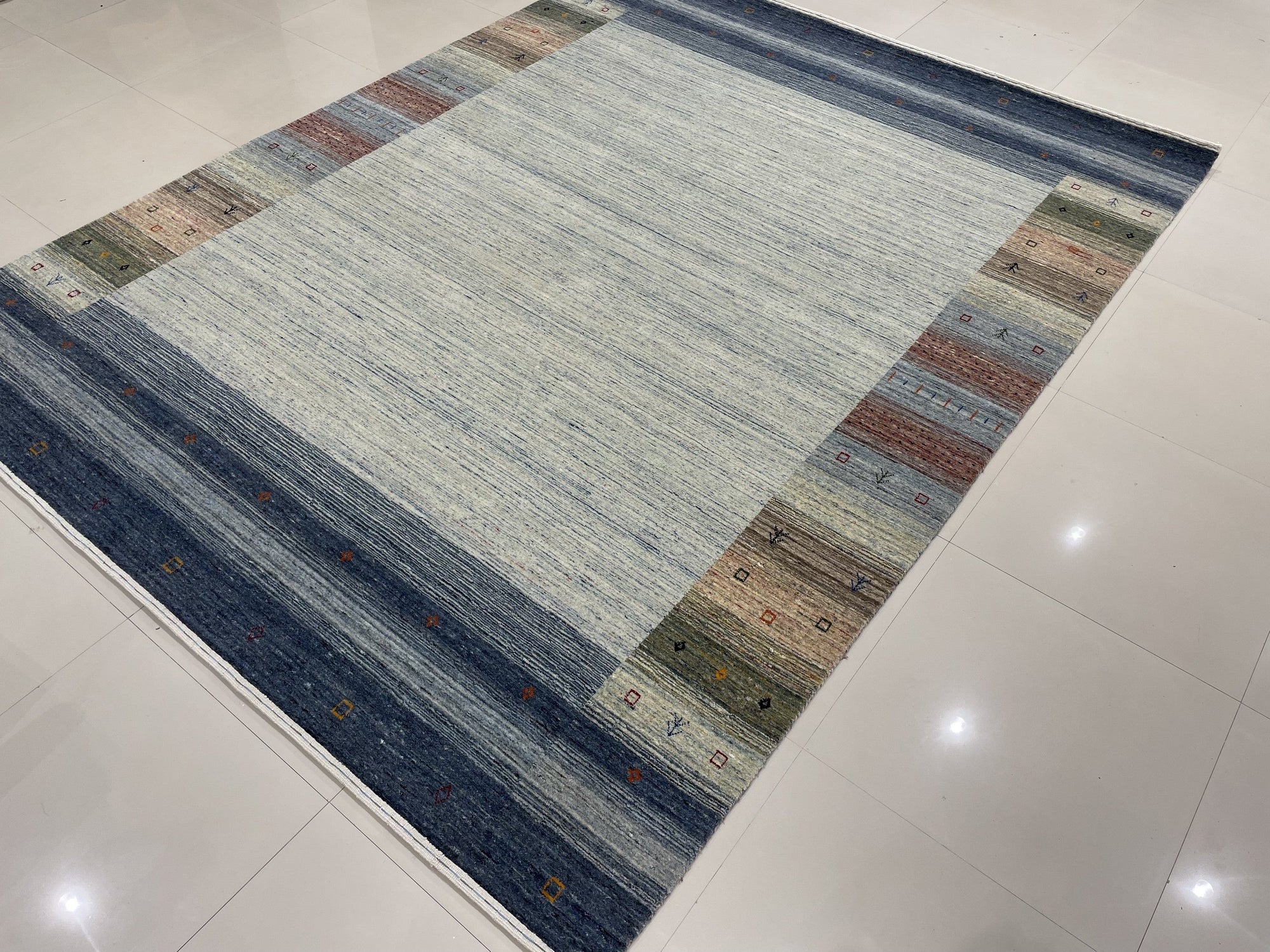 Chic Gabbeh Gray Handmade Wool Rug, a textured gray wool rug with a minimalist design, lies flat on a light surface, showcasing its subtle variations in tone and hand-knotted construction.