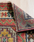 Lydia Kazak Brown Hand Knotted Wool Rug, its warm brown hues and intricate Kazak design grounding a warmly lit living space. Hand-knotted wool construction adds texture and depth.