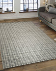Sumptuous Jade Beige Handmade Wool & Viscose Rug, displaying a subtle sheen and intricate weave, rests elegantly on a dark wood floor, its soft palette complementing a minimalist space.