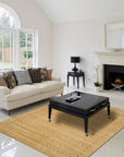 Jasmine Alluring Beige Handmade Wool Rug gracing a warmly lit living room. Soft beige tones and intricate wool texture complement the minimalist furniture and decor, creating a serene and inviting space.