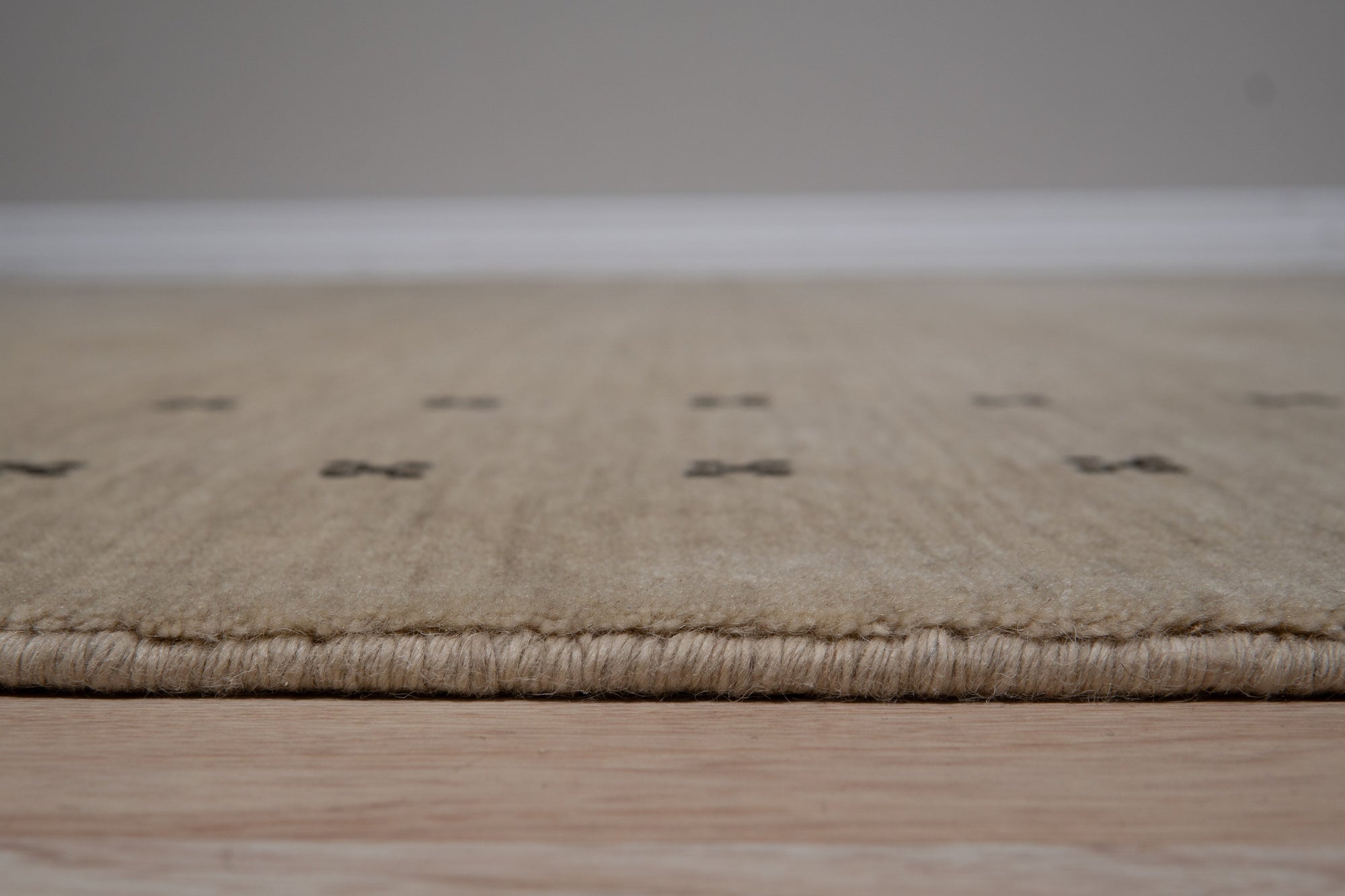 Jasmine Alluring Beige Handmade Wool Rug displayed on a polished hardwood floor, its subtle beige hues and wool texture adding warmth and sophistication to the light-filled space.