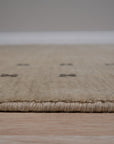 Jasmine Alluring Beige Handmade Wool Rug displayed on a polished hardwood floor, its subtle beige hues and wool texture adding warmth and sophistication to the light-filled space.