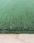 Jasmine Alluring Green Handmade Wool Rug graces a modern living space, its verdant hues complementing neutral furniture. Hand-knotted wool construction provides texture and warmth underfoot.