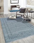 Jasmine Alluring Gray Handmade Wool Rug graces a modern living room; its soft gray tones complementing a white sofa and light wood flooring, creating a serene and inviting atmosphere.