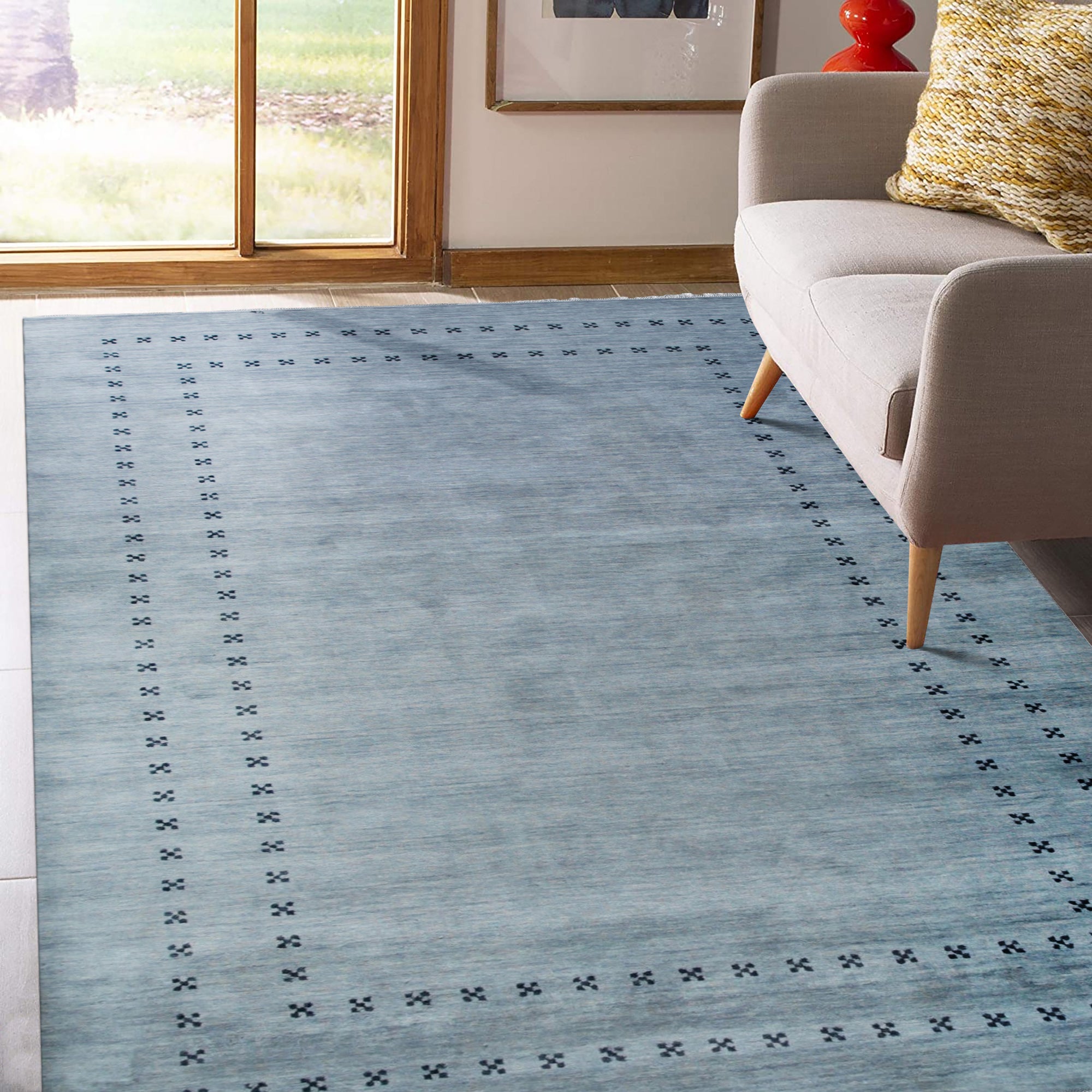 Jasmine Alluring Gray Handmade Wool Rug displayed in a softly lit living room. Gray hues blend across its wool texture, contrasting subtly with a light wooden floor. Corner of a mid-century modern chair adds scale.