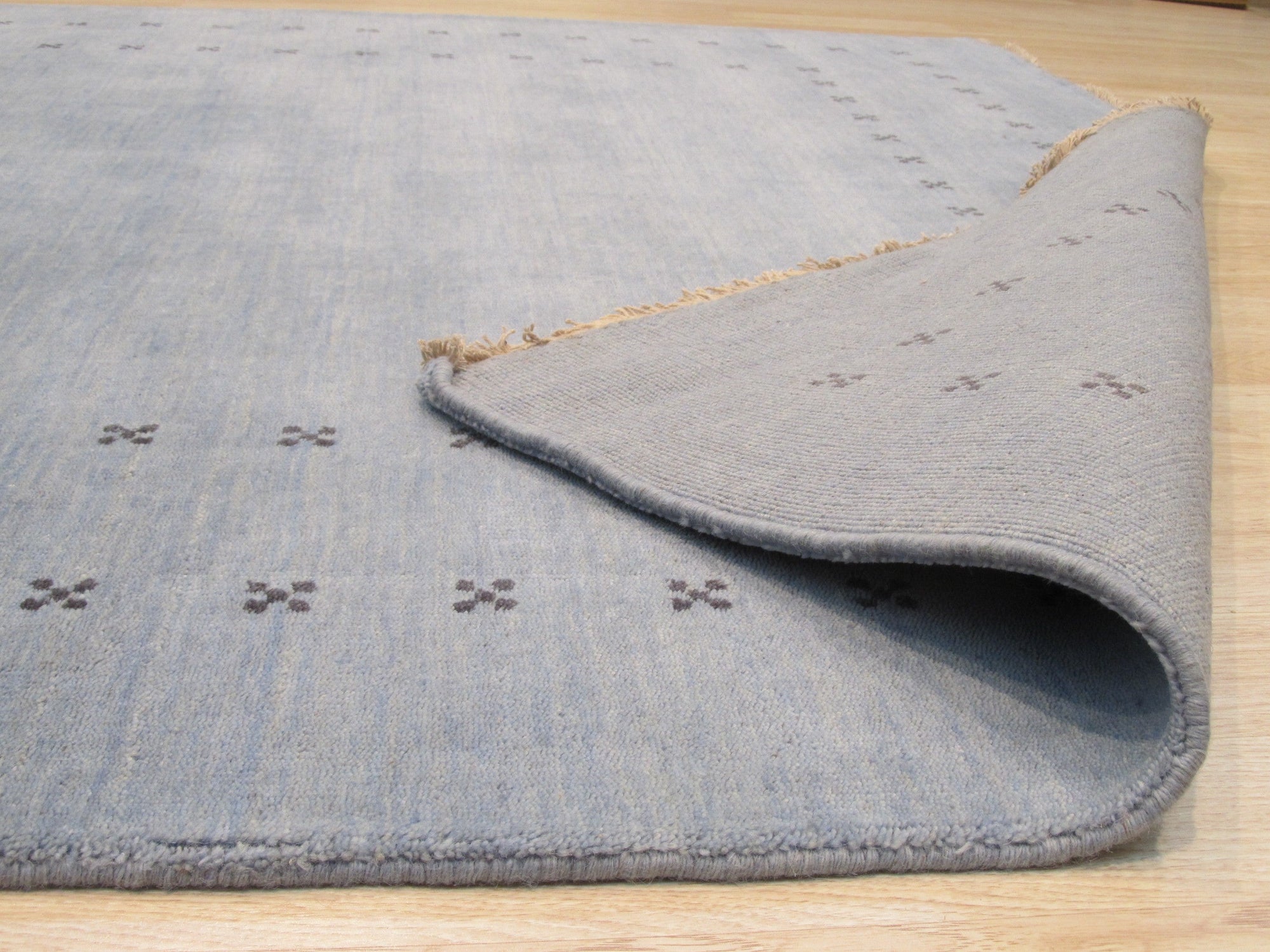 Jasmine Alluring Light Blue Handmade Wool Rug graces a bright living room; light dances across the rug’s subtle pattern woven in soft light blue wool, creating a serene and inviting space.