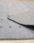 Jasmine Alluring Light Blue Handmade Wool Rug graces a bright living room; light dances across the rug’s subtle pattern woven in soft light blue wool, creating a serene and inviting space.