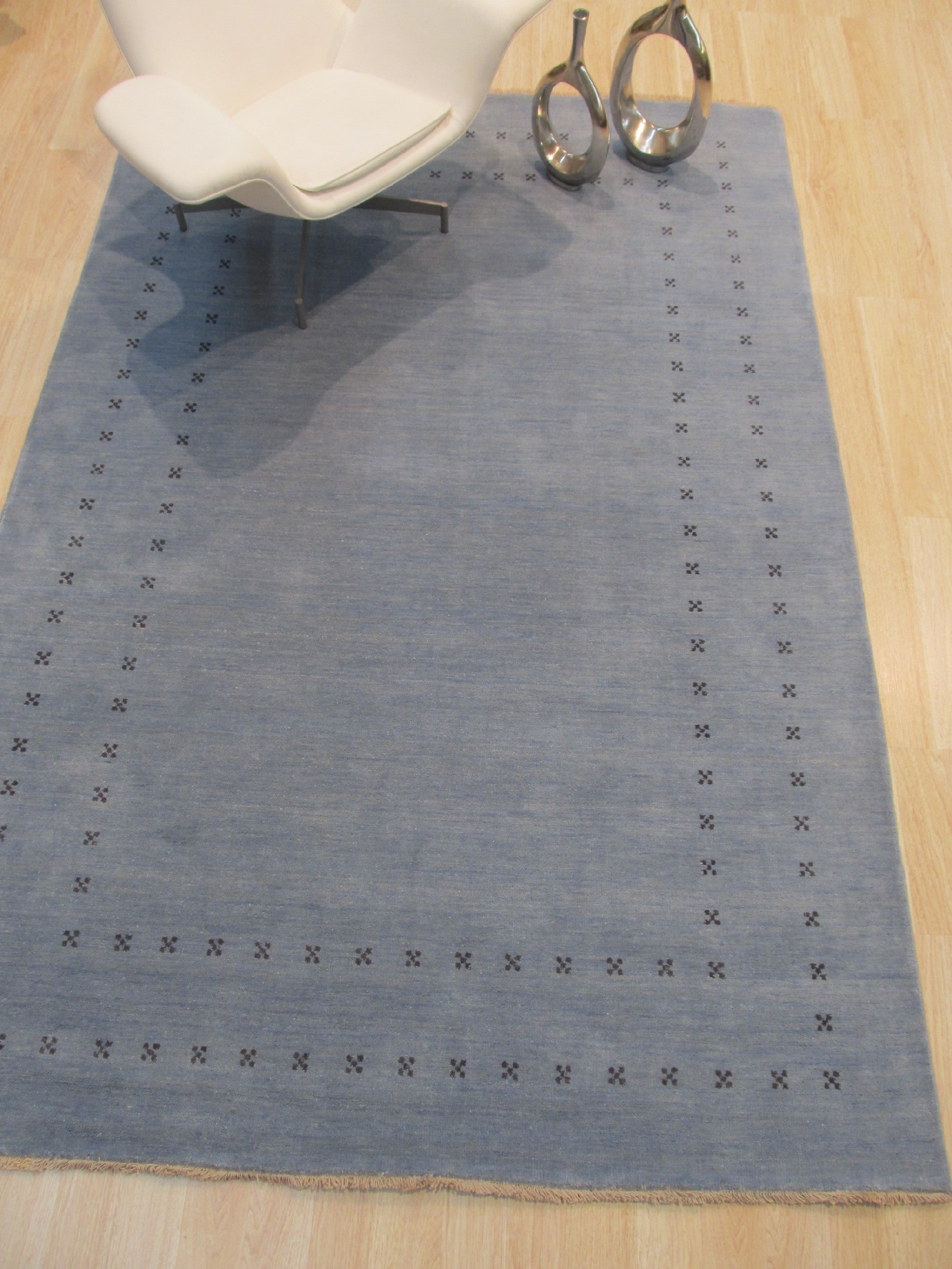 Jasmine Alluring Light Blue Handmade Wool Rug graces a bright, stylish living room. Soft light washes over the rug’s intricate pattern and gentle light blue hue, highlighting its handcrafted wool texture beneath a minimalist coffee table and modern furniture.