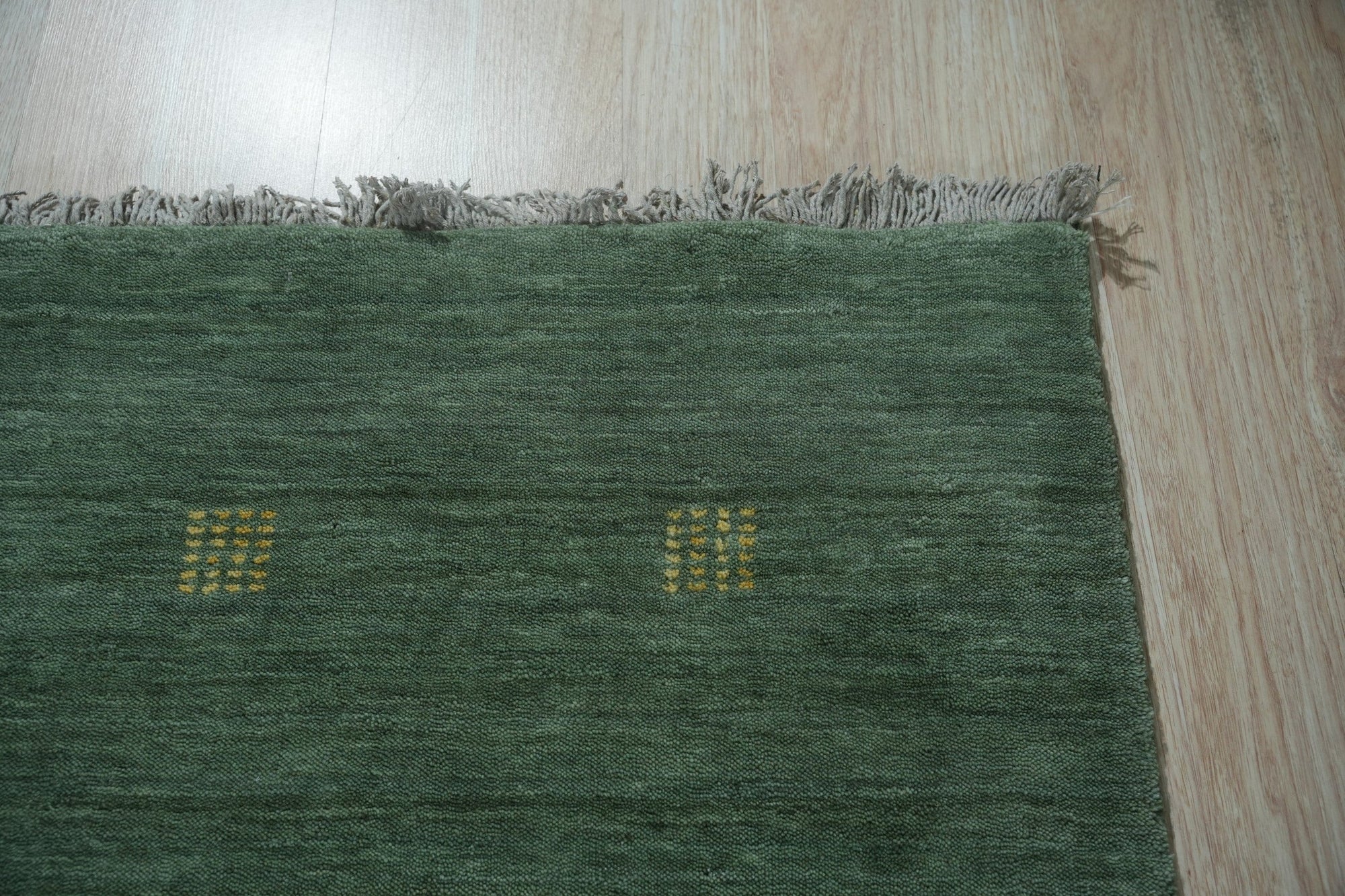 Laine Amara Green Handmade Wool Rug, its textured wool surface a vibrant green, lies on a light wood floor, showcasing its organic, flowing design and handmade construction.