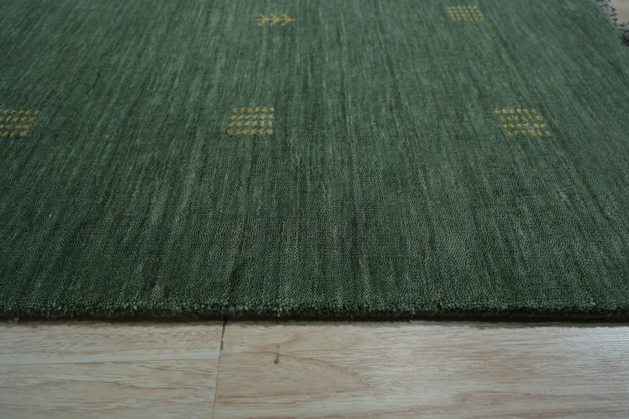 Laine Amara Green Handmade Wool Rug, seen in a bright, inviting living room. The rug's textured wool pile adds warmth to the light wood flooring, complementing the neutral furniture and potted plant.